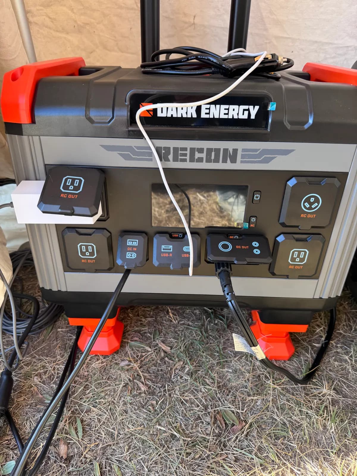 A Dark Energy Recon portable power station with cords plugged into its outlets.